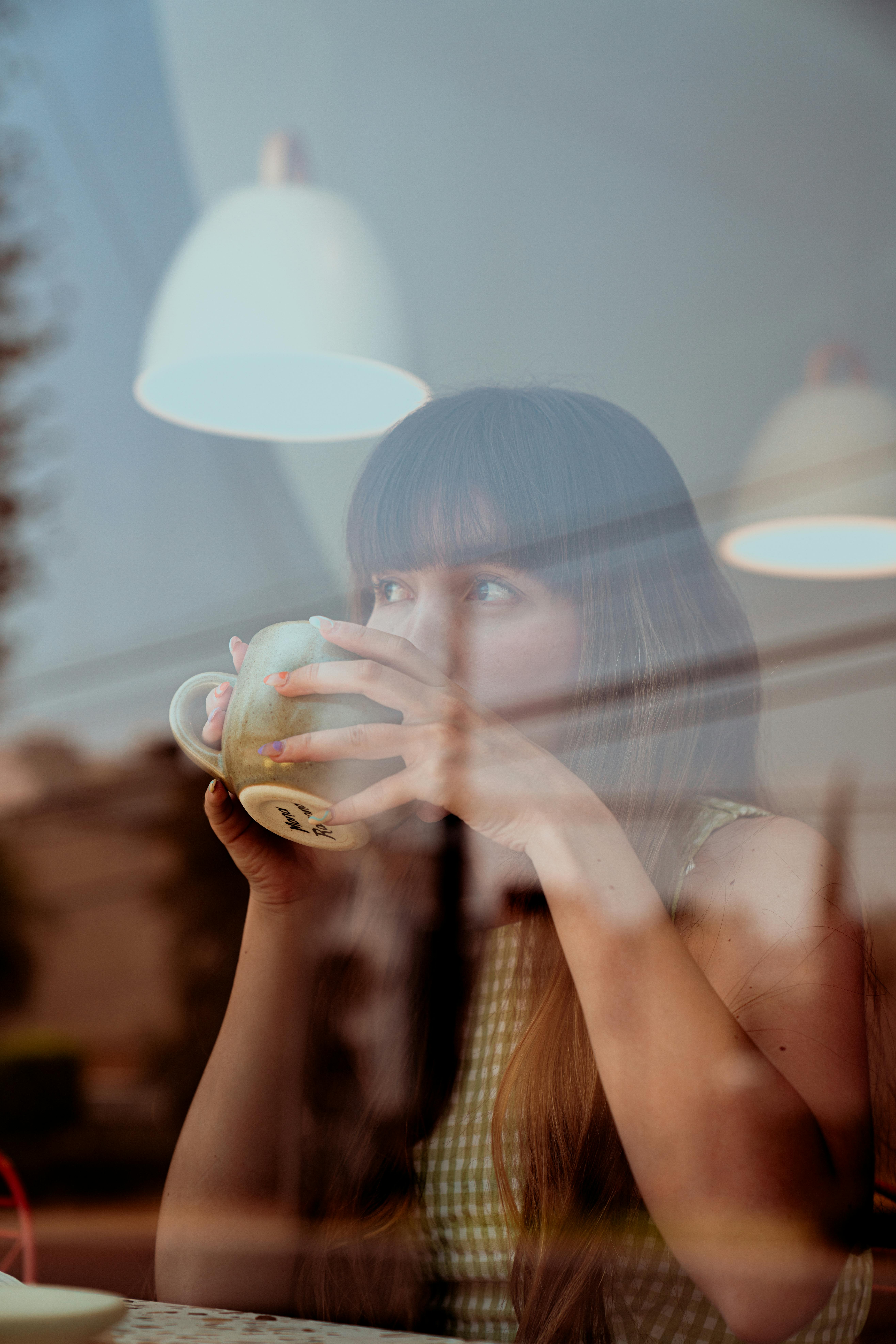 Menina toma café em frente a janela